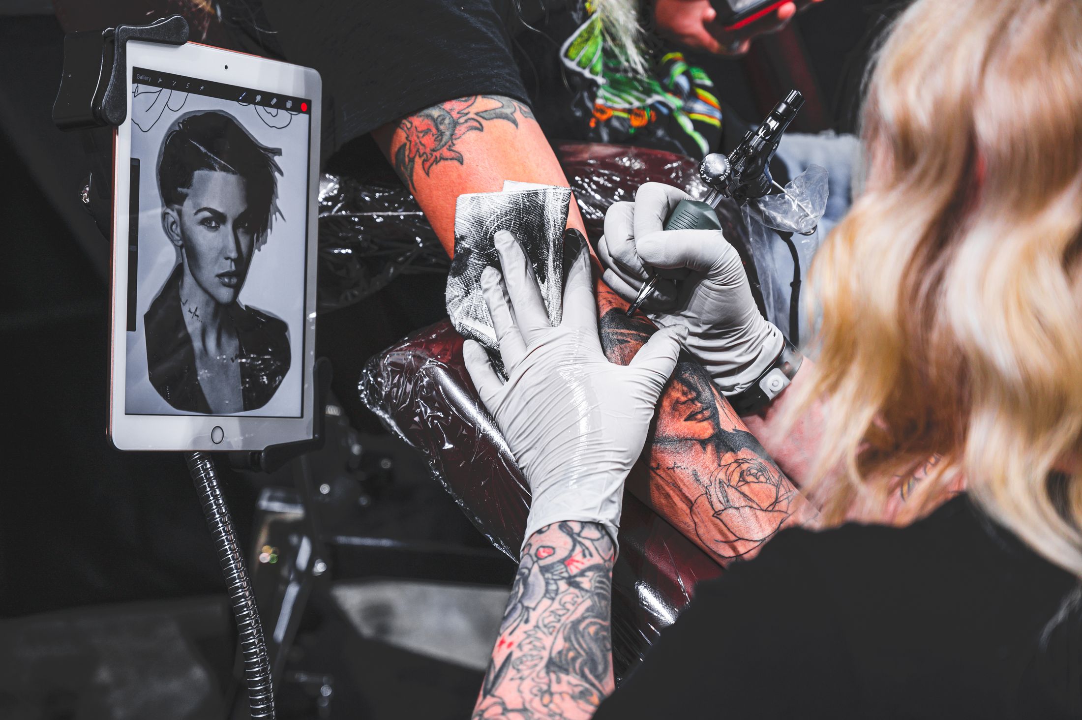 Gloved tattoo artist shading a detailed black-and-grey portrait tattoo during a real studio session